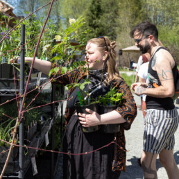 Shoppers selecting native plants at Oxbow’s Plant Stand, carrying potted plants for sustainable gardening and habitat restoration.